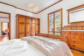 Une chambre avec un grand lit, une armoire en bois et une fenêtre donnant sur les arbres.