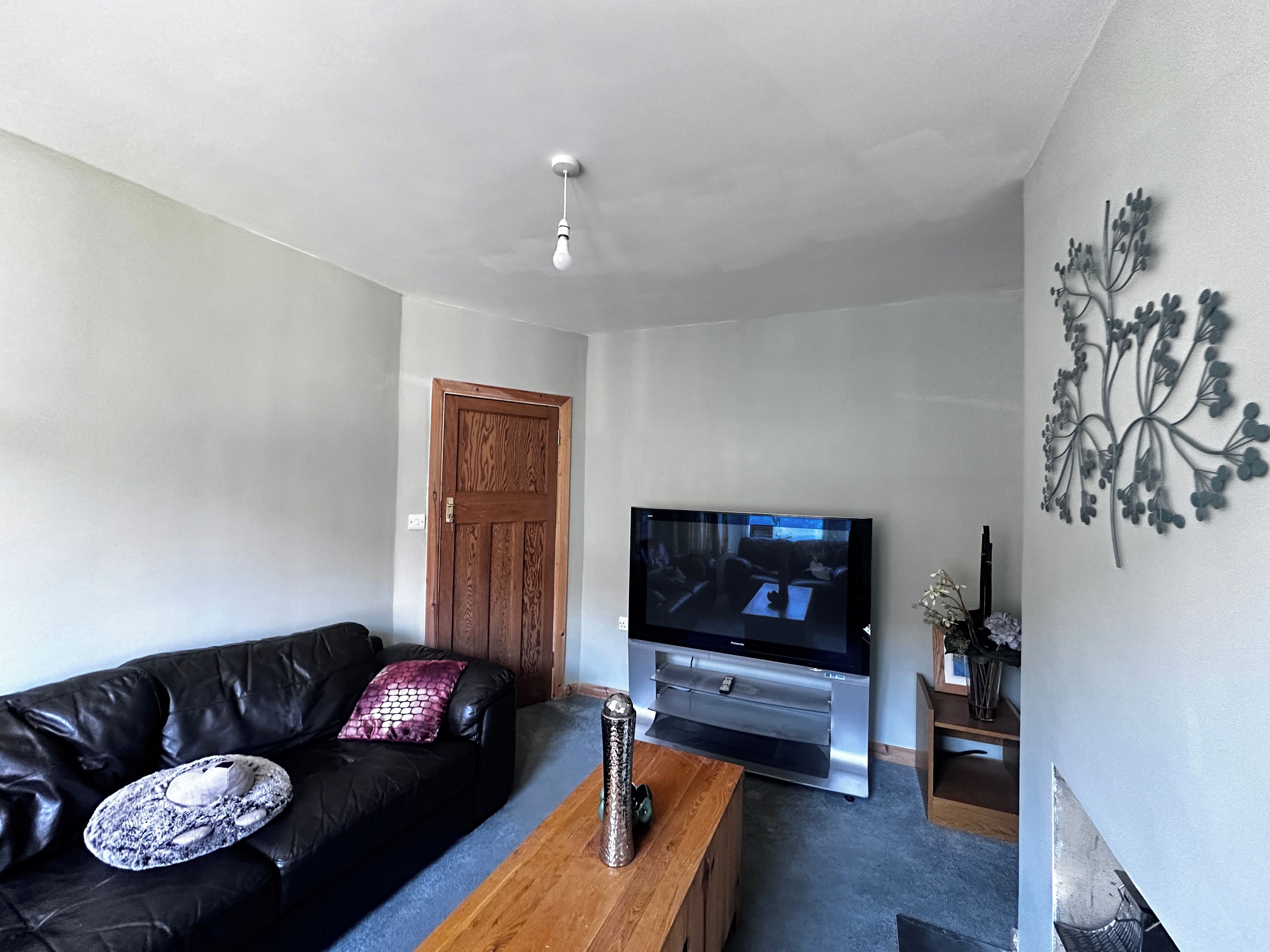 Una sala de estar con un sofá de cuero negro, una mesa de centro de madera, un televisor de pantalla plana y un elemento decorativo en la pared.