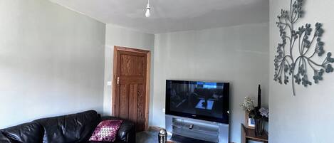 Una sala de estar con un sofá de cuero negro, una mesa de centro de madera, un televisor de pantalla plana y un elemento decorativo en la pared.