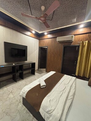 Ein Hotelzimmer mit Bett, Wandfernseher, Deckenventilator und Klimaanlage.