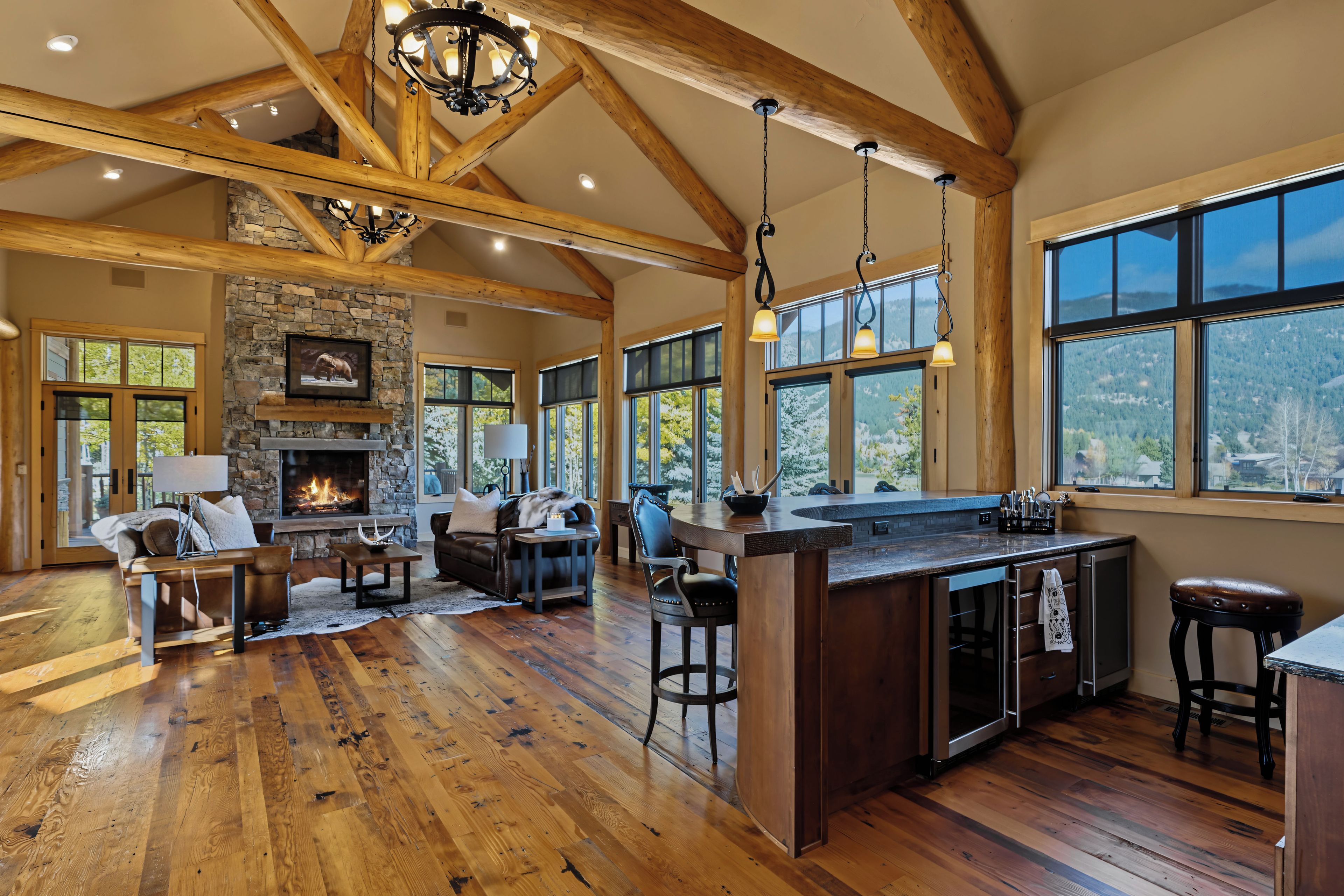 A spacious living area with a fireplace, wooden beams, and large windows offering a view of the outdoors.
