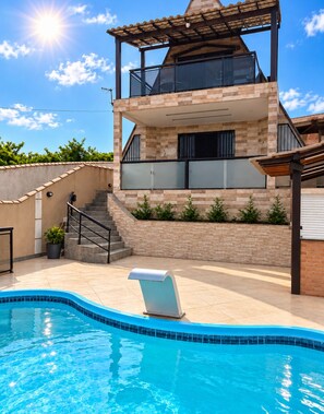 A modern two-story house with a swimming pool, a covered patio, and a staircase leading to the upper level.
