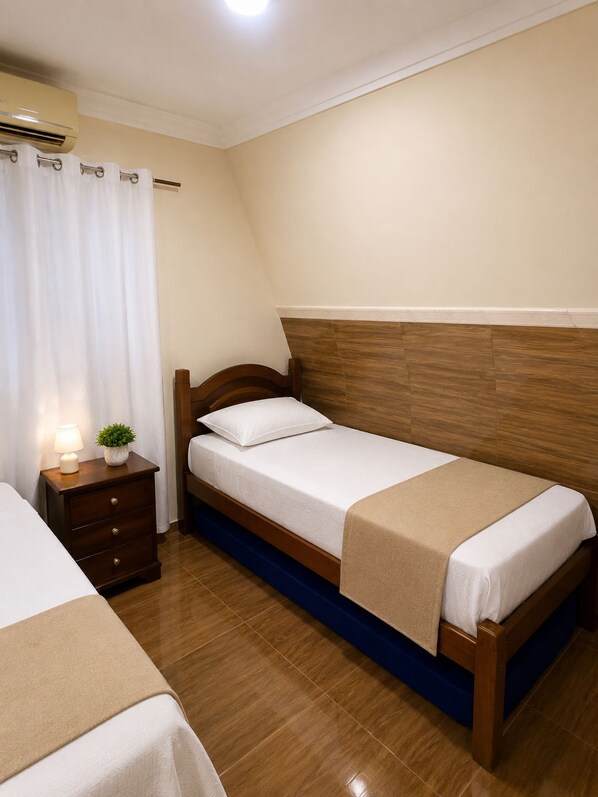 A hotel room with two beds, a nightstand with a lamp and a plant, and a wooden headboard.