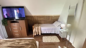 Una habitació d'hotel amb un llit, una taula de nit amb una làmpada, un televisor sobre un moble de fusta i una catifa petita a terra.