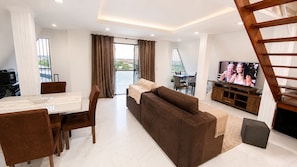 A modern living room with a sofa, dining table, chairs, a TV, and a staircase.