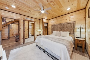 Une chambre dans une cabane en bois, comprenant un lit, une table de chevet, un ventilateur de plafond et un panneau indiquant l’emplacement des toilettes.