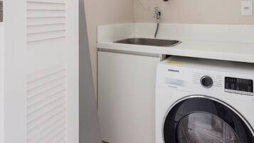 Een kleine wasruimte met een wasmachine, een wastafel en een boiler.