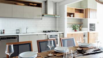 Een moderne keuken met witte kasten, een eettafel met borden en glazen, en gevlochten hanglampen.