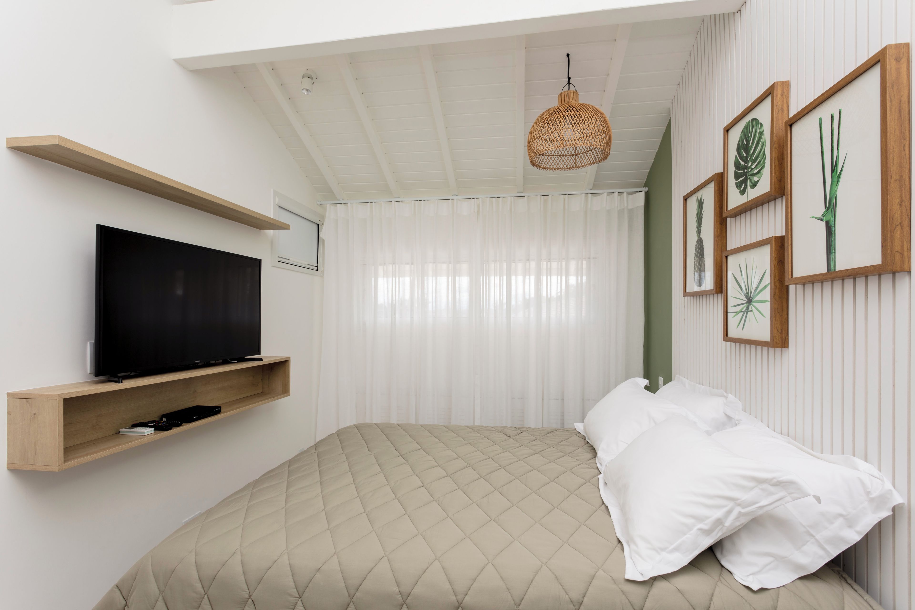 A bedroom with a bed, a TV on a shelf, a hanging light, and framed pictures on the wall.