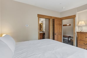 Habitació d'hotel amb llit, un armari de fusta, escriptori amb làmpada i un bany visible a través d'una porta oberta.