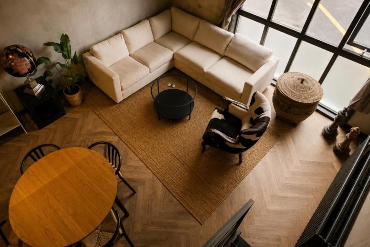 Un salon moderne avec un canapé d’angle, une table ronde en bois et une grande fenêtre.