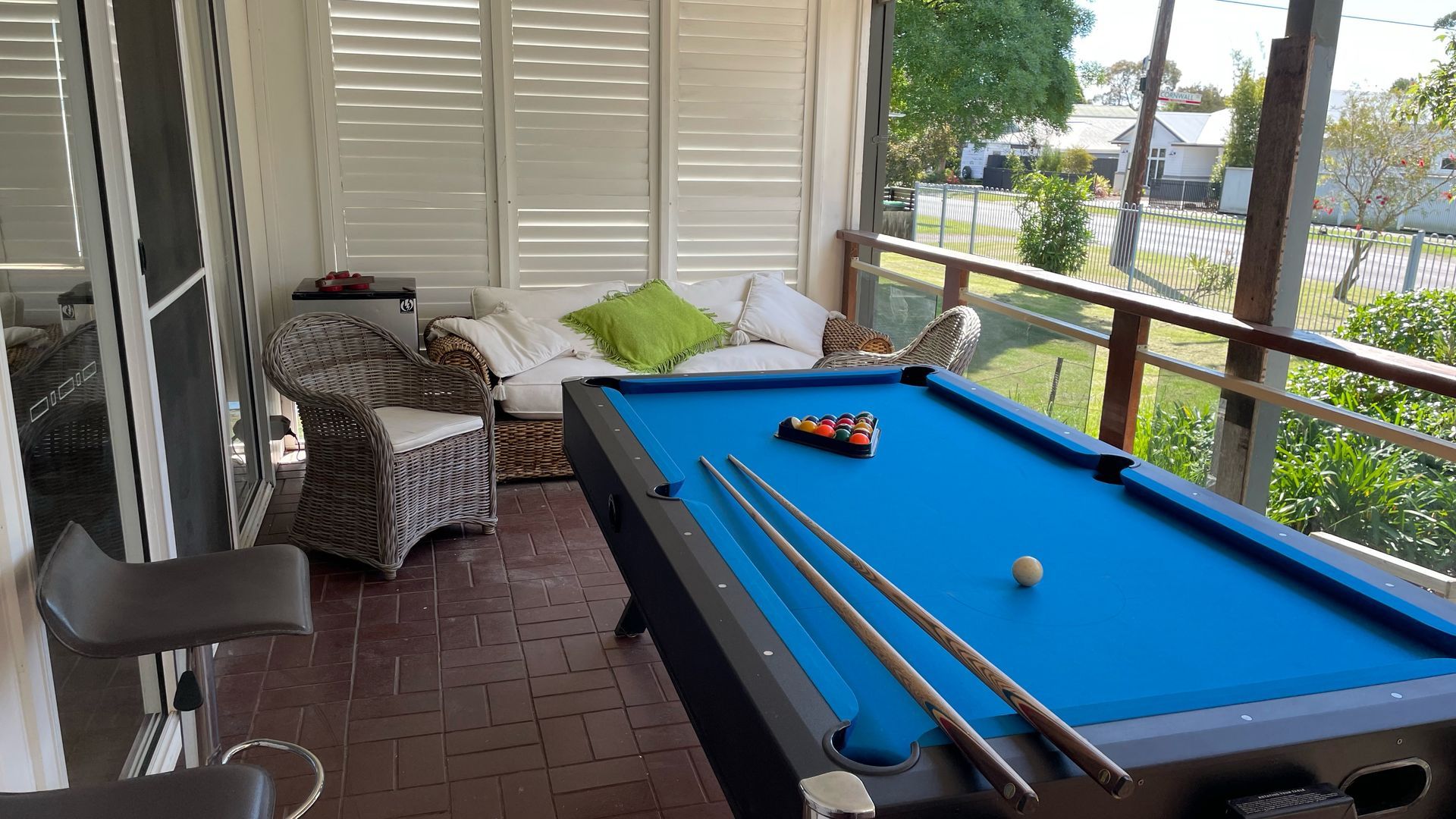 Ein Billardtisch mit grüner Spielvliesfläche, umgeben von Korbmöbeln und einem Glasgeländer.