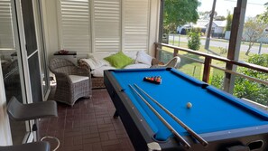 Een pooltafel met een groene viltkleed, omringd door rieten meubels en een glazen balustrade.