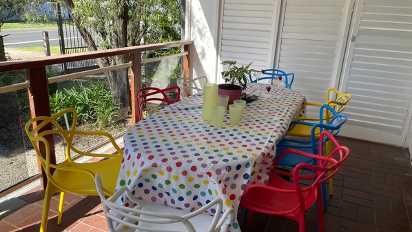 An outdoor patio with a table set for two, surrounded by colorful chairs, a potted plant, and a glass of wine. - Super Cool Retro Shack (Cowes)