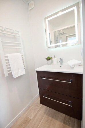 A modern bathroom with a white vanity, a mirror, a towel rack, and a small potted plant. - New Listing (Saint-Germain-de-Lusignan)