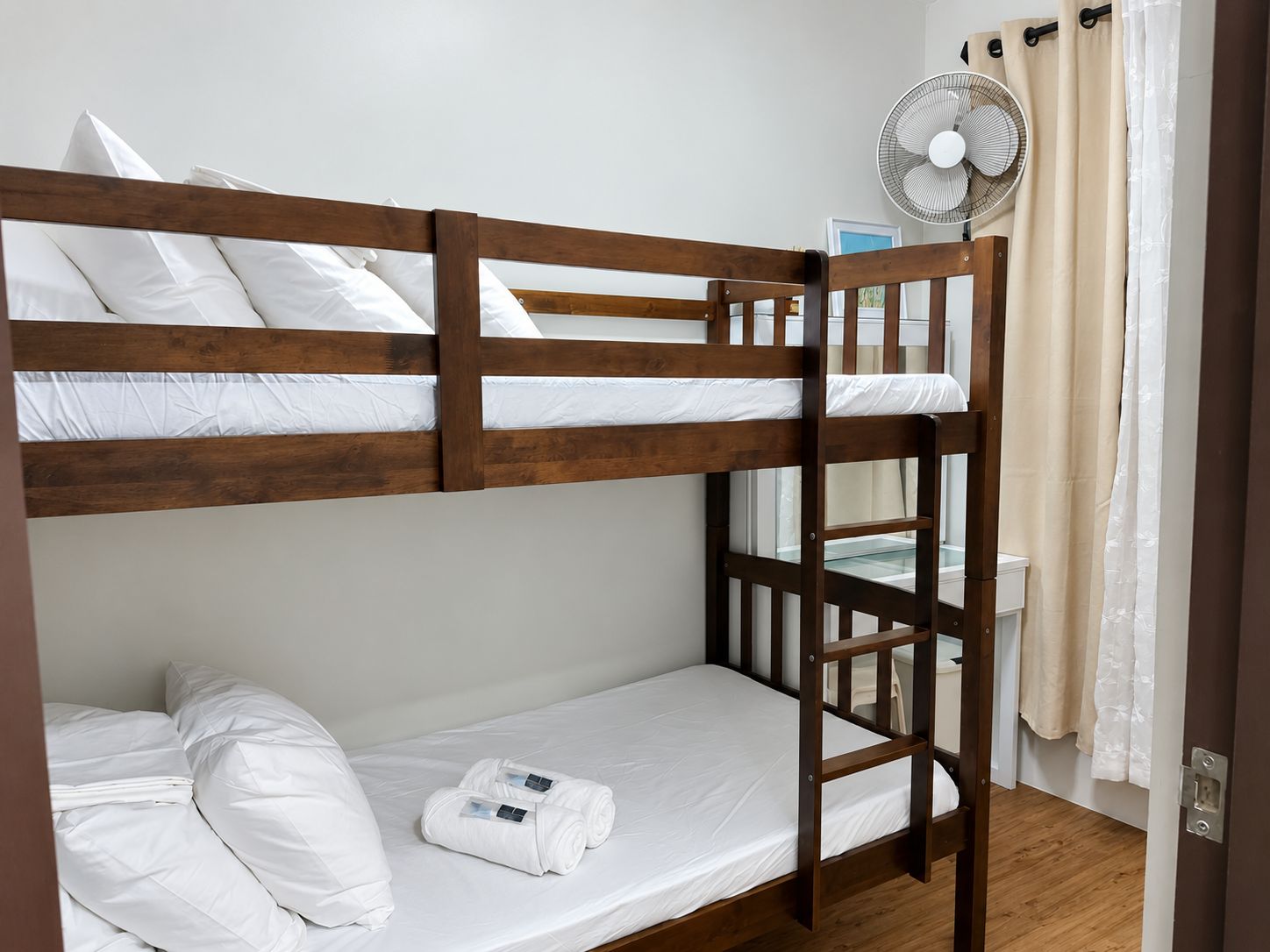 A bunk bed with white bedding and a fan on the upper bunk.