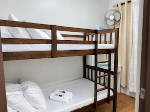 A bunk bed with white bedding and a fan on the upper bunk.