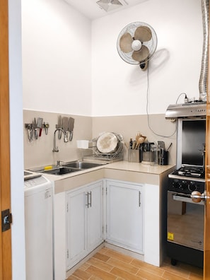 A compact kitchen with a built-in stove, a dish drying rack, and a wall-mounted fan.