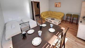 Ein Zimmer mit einem Bett, einem gelben Sofa, einem Esstisch mit Stühlen und einer kleinen Küchenzeile.