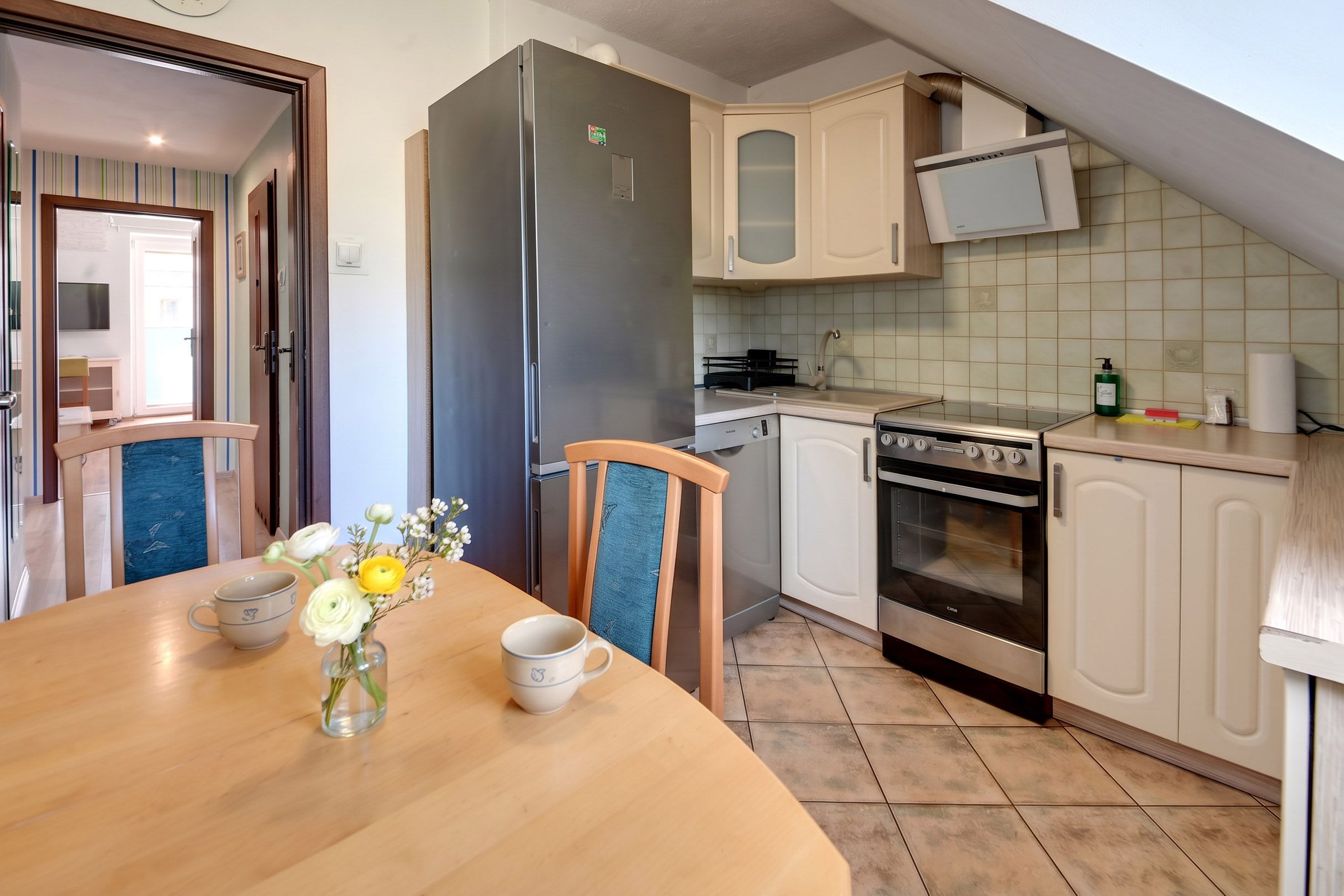 A compact kitchen with a refrigerator, oven, and microwave. There is a dining table with chairs and a vase with flowers.