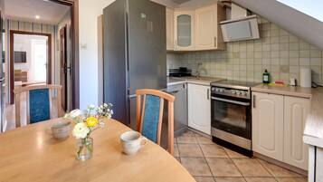 A compact kitchen with a refrigerator, oven, and microwave. There is a dining table with chairs and a vase with flowers.