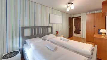 Une chambre d’hôtel avec deux lits, une table de chevet agrémentée d’un vase, une armoire et un miroir.
