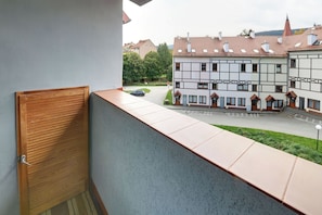 Een balkon met een houten deur, een betonnen rand en uitzicht op een woonstraat met huizen en een auto.