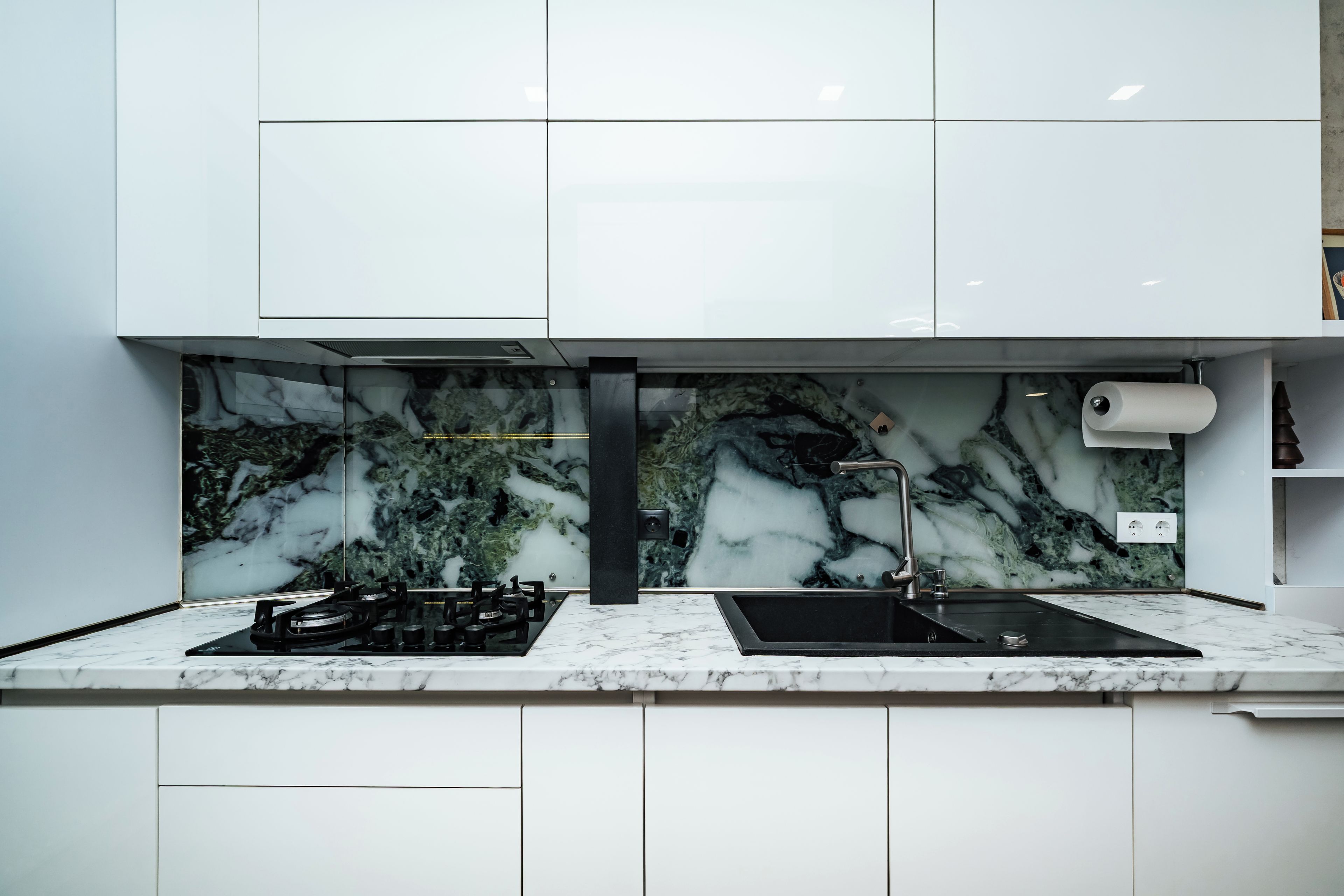 A modern kitchen with a marble backsplash, a gas stove, and a sink.