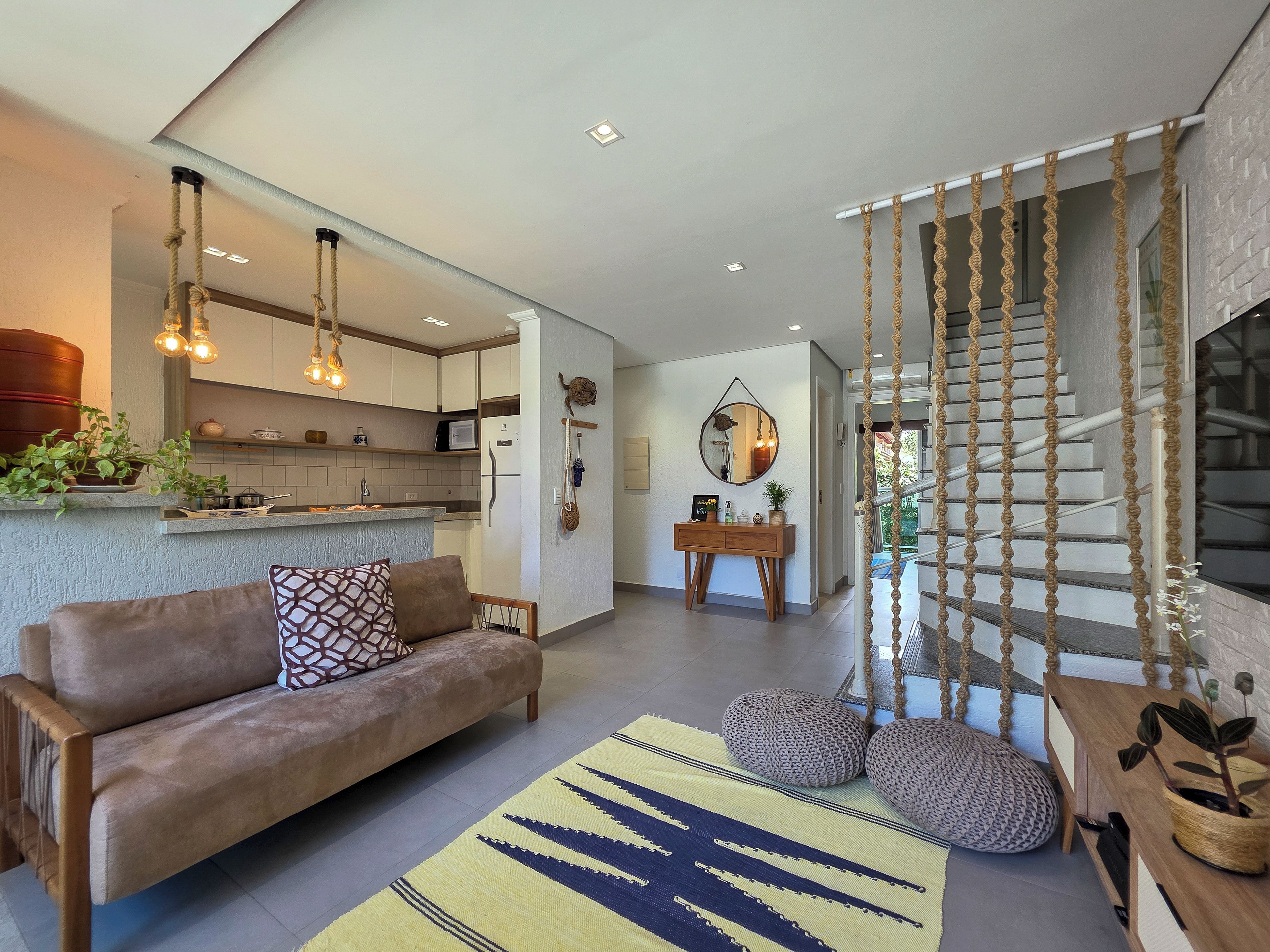 A modern living space with a sofa, a rug, a staircase with rope decor, and a kitchen area.