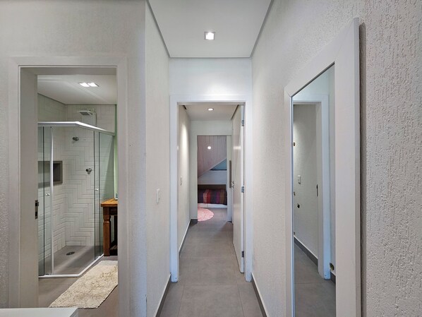 A hallway with a glass shower enclosure, a wooden bench, and a rug. - Sabel Residence 14 (Bertioga)