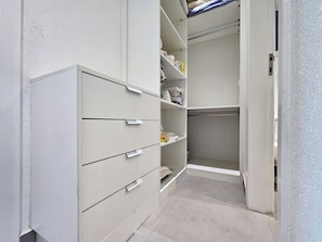 Ein begehbarer Kleiderschrank mit offenen Regalen und Schubladen, einer Kleiderstange und einer Tür zu einem anderen Raum.