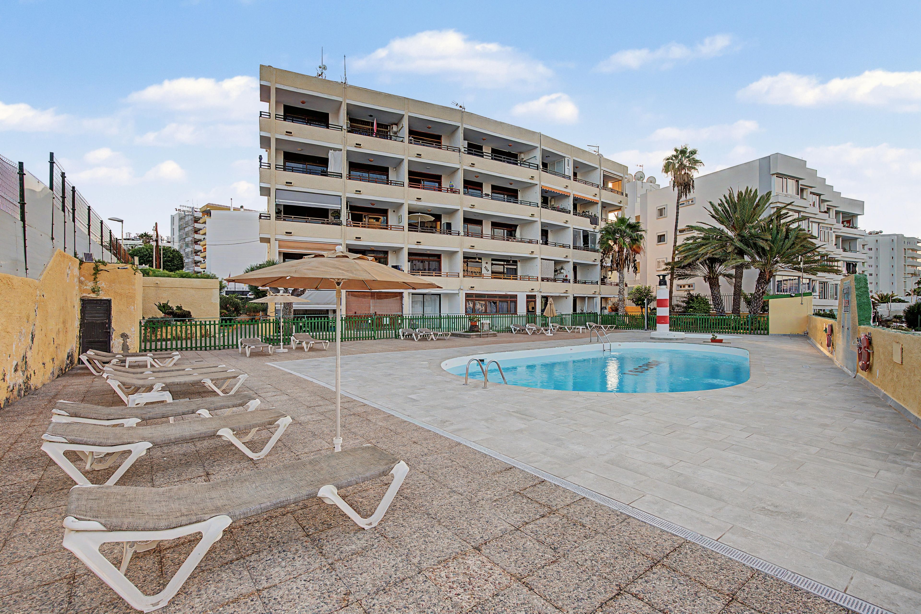 Un hotel de varios pisos con piscina, sillones de descanso y un patio amurallado.