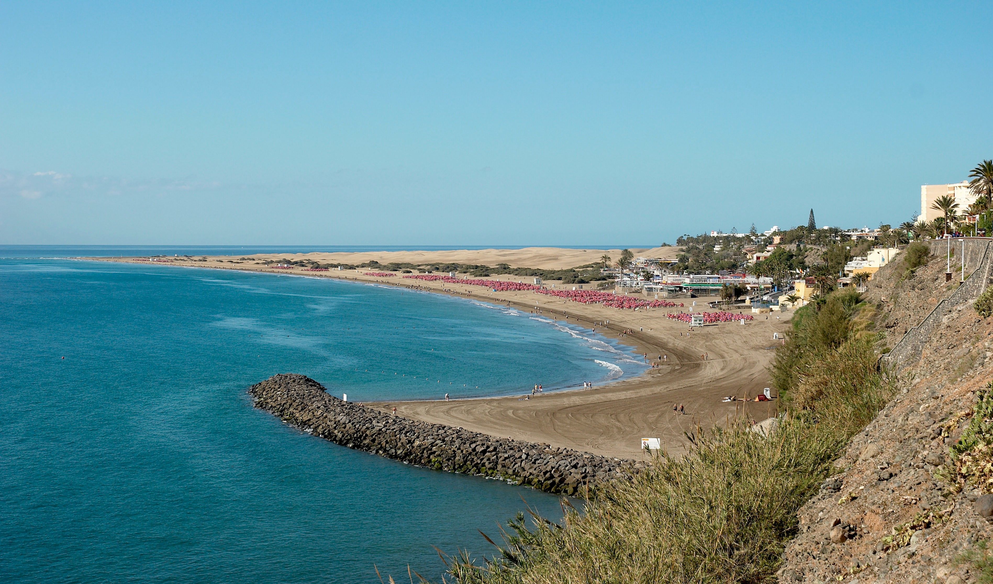 Une scène de plage côtière avec une digue rocheuse, une plage de sable et une ville en arrière-plan.