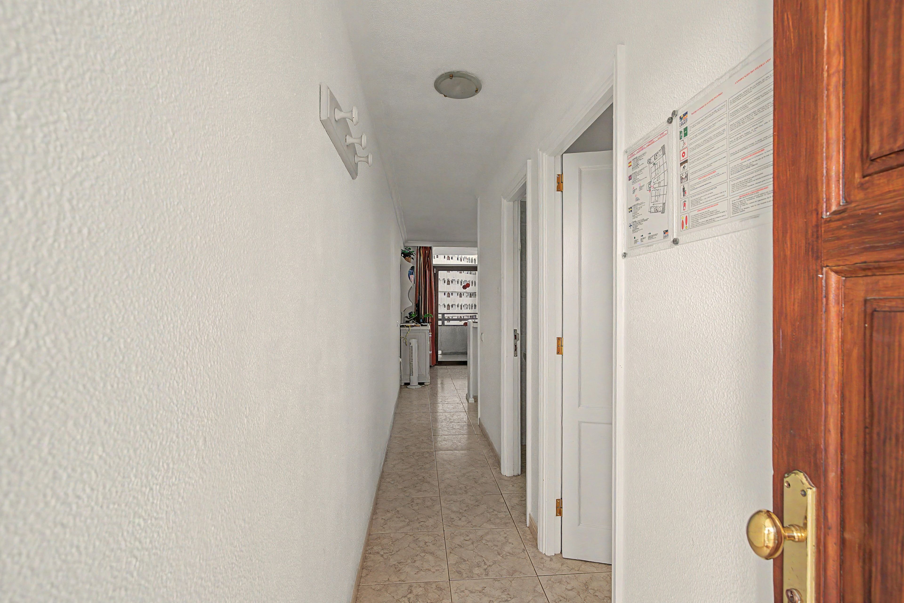 Un pasillo con paredes blancas, piso de baldosas y una puerta con picaporte de latón.