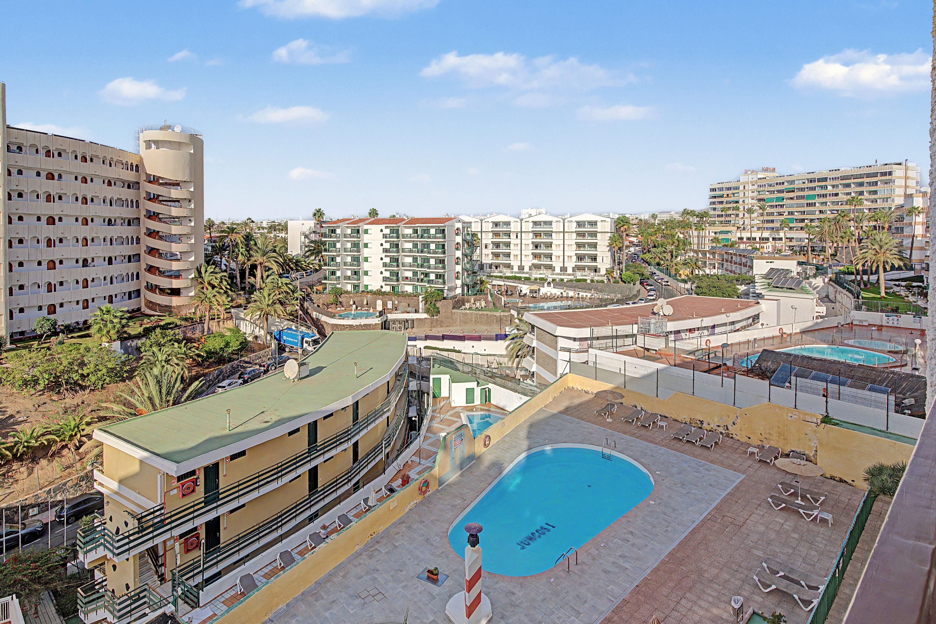 Un resort con múltiples piscinas, un edificio grande con balcones y un cielo despejado.