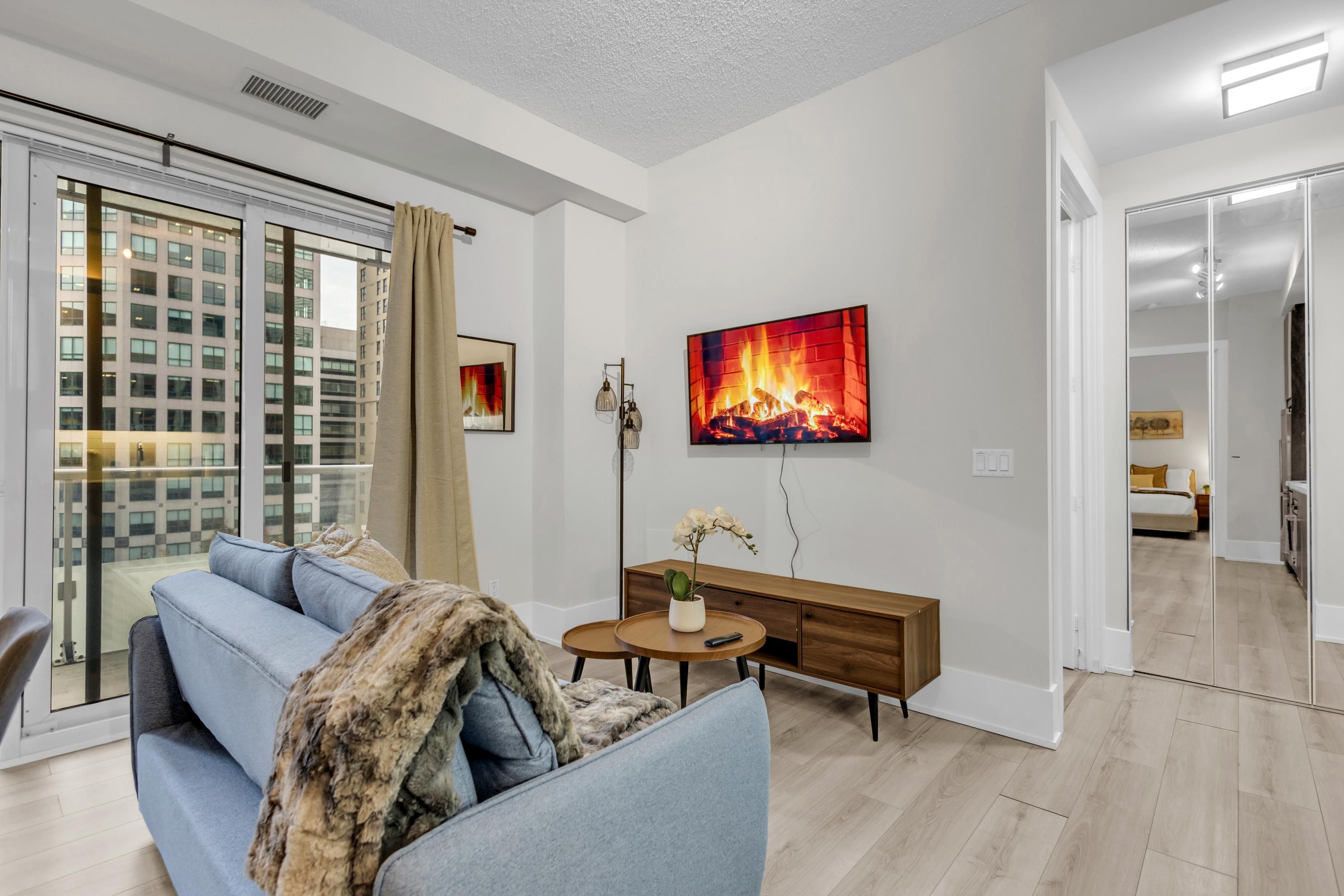 A modern living room with a sofa, a small round table, a wooden console, and a fireplace painting.