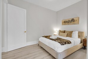 Un dormitorio con cama, mesita de noche, lámpara de pared y una puerta.
