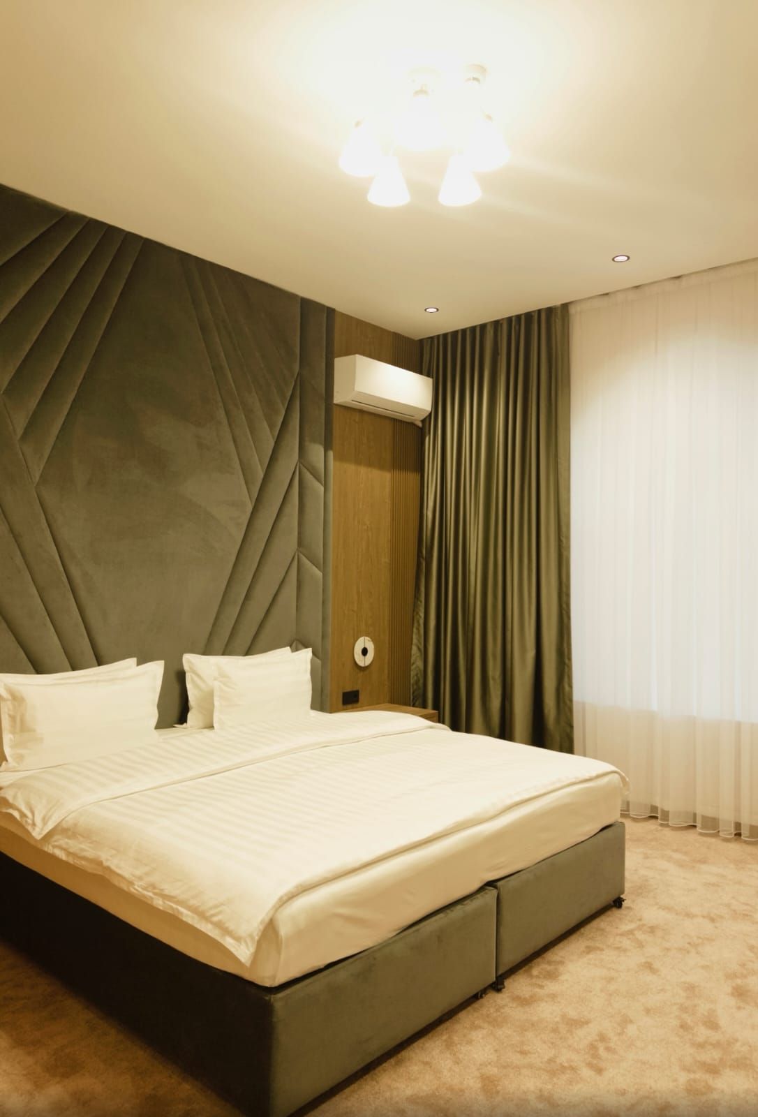Una camera d'albergo moderna con un letto grande, un condizionatore d'aria a parete e una finestra con tende.