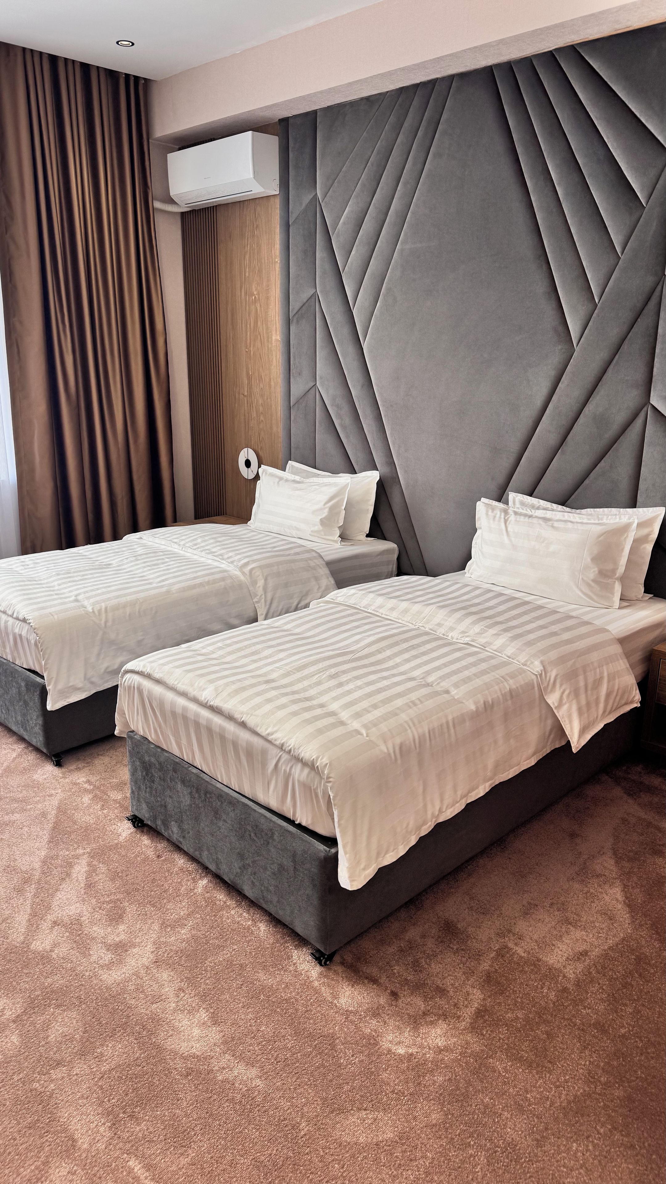 Quarto de hotel com duas camas, unidade de ar condicionado de parede grande e design de parede texturizado.