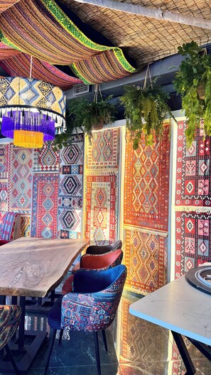 A dining area with a wooden table and chairs, surrounded by walls adorned with patterned textiles. - Karavan Palace Hotel (Turkestan)