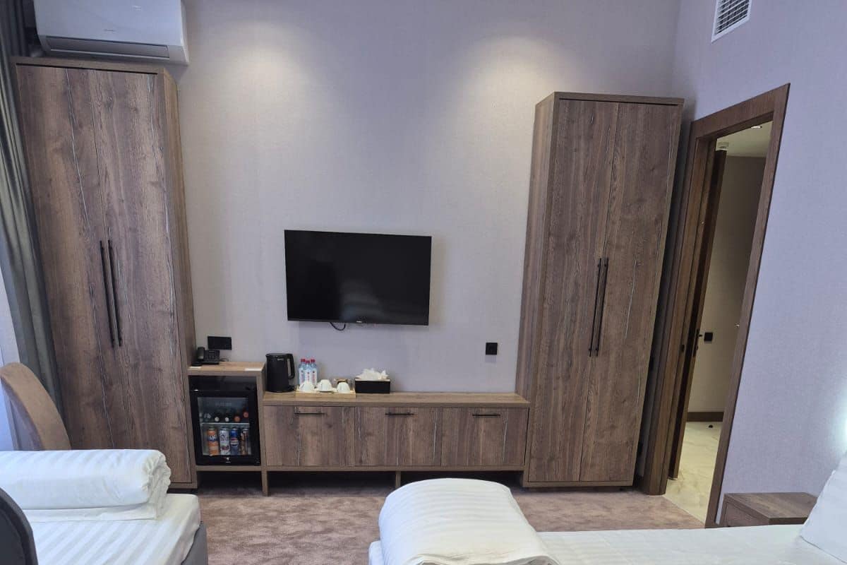 A hotel room with two beds, a TV, a minibar, and wooden wardrobes.