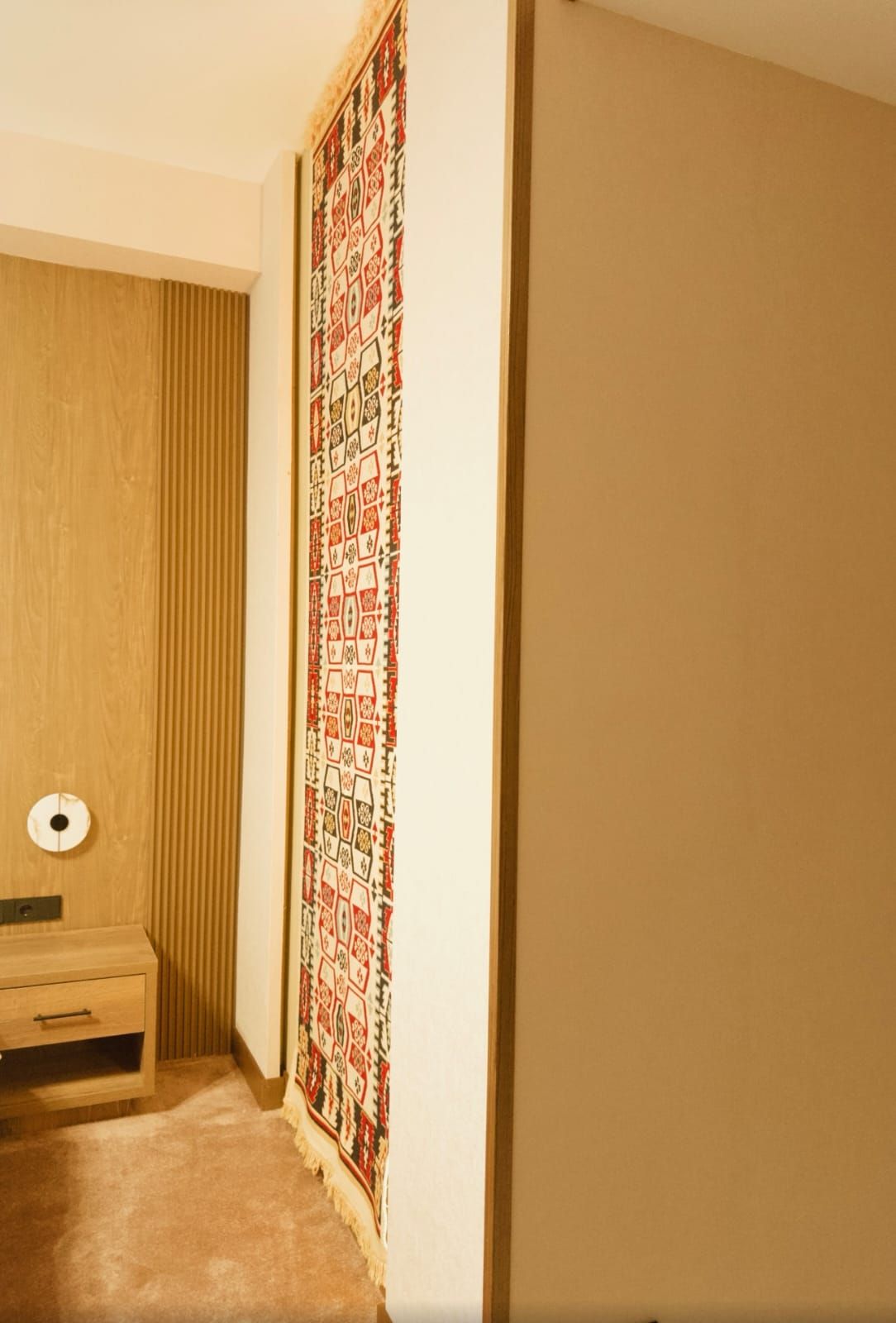 Una habitación con una puerta de madera, un tapiz estampado y un pequeño armario de madera con luz.