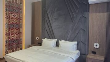 Una habitación de hotel moderna con una cama grande, un panel decorativo en la pared, una cortina estampada y una mesita de noche pequeña.