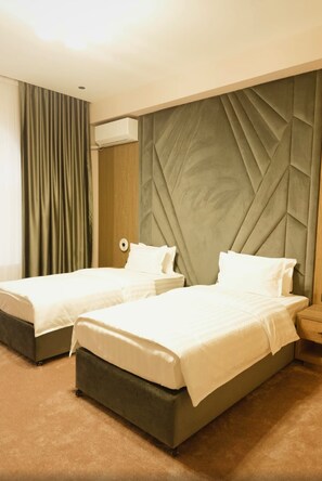 A hotel room with two beds, a large padded headboard, and a wooden accent wall. - Karavan Palace Hotel (Turkestan)
