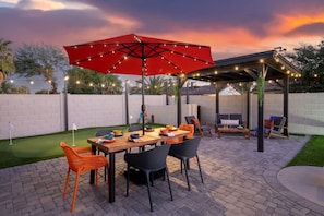 Une terrasse extérieure avec une table, des chaises et un parasol rouge.