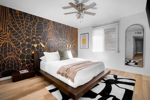 Une chambre moderne avec un lit, un ventilateur de plafond, un grand miroir et un mur décoré d’un motif.