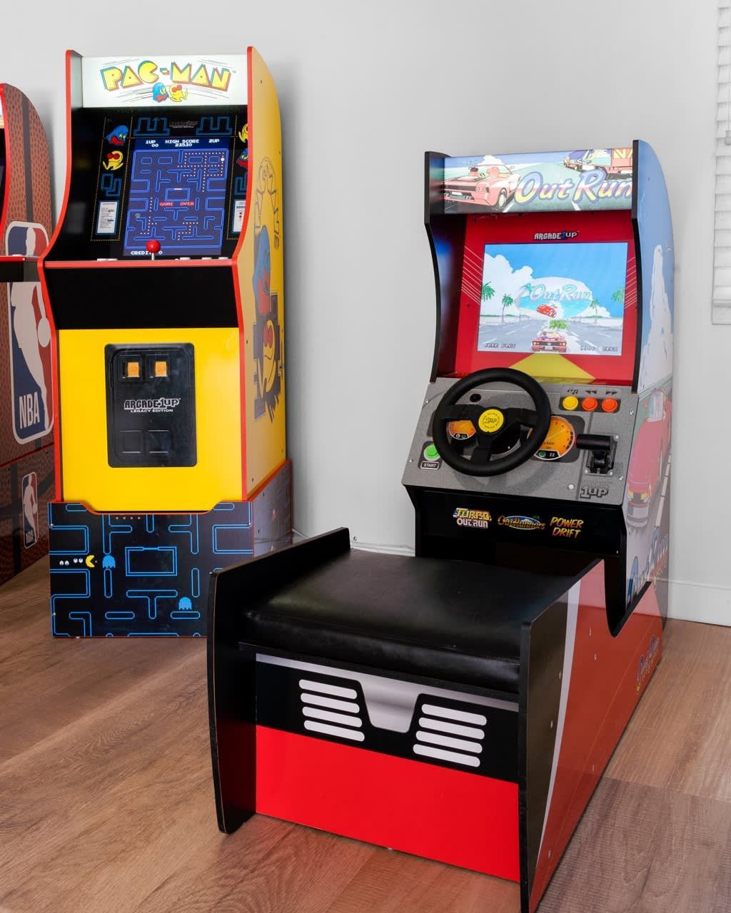 Deux bornes d’arcade, l’une portant l’inscription « PAC-MAN » et l’autre « Out Run », sont placées sur un plancher en bois.