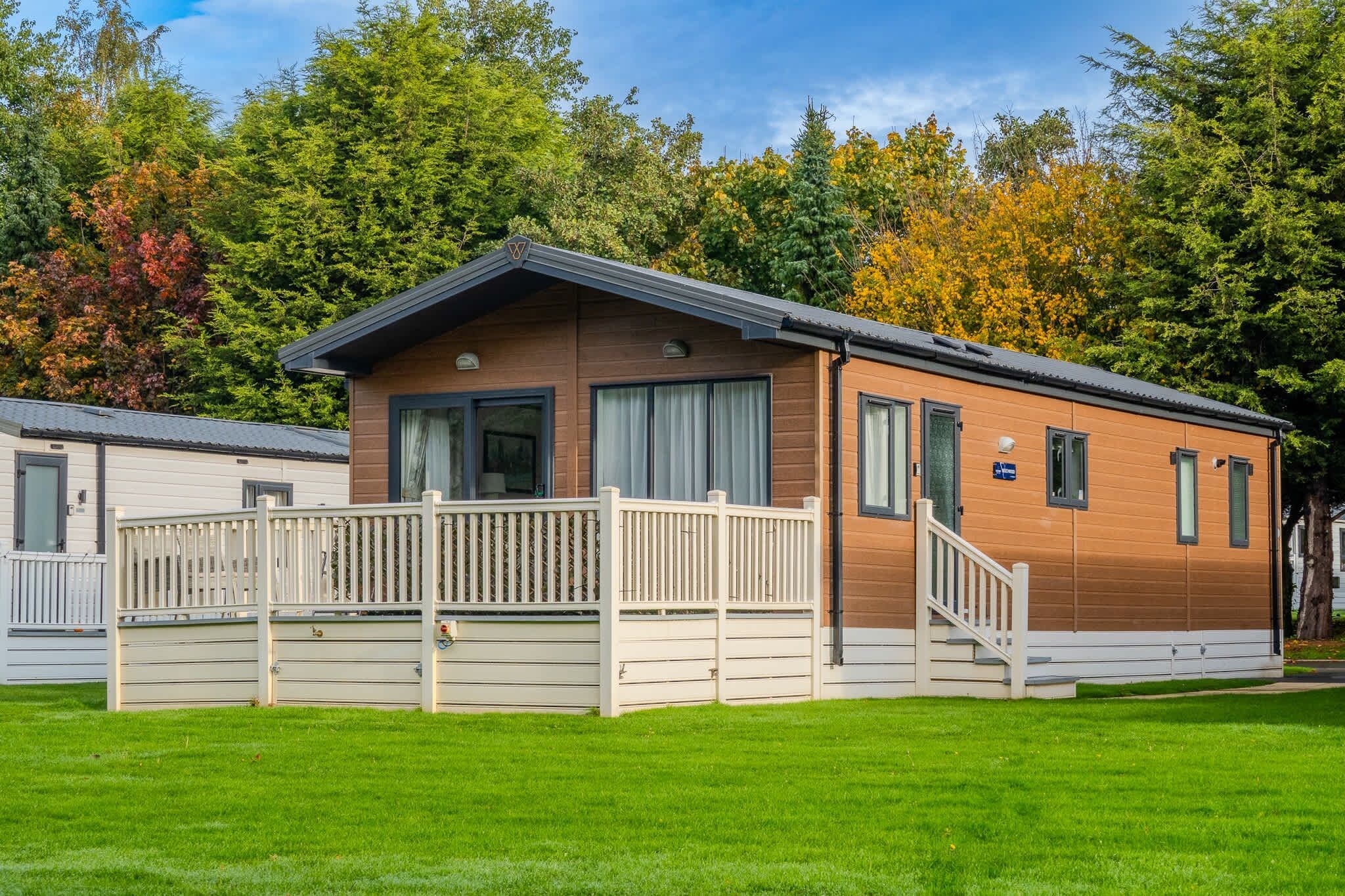 A single-story wooden cabin with a balcony, surrounded by a well-maintained lawn and trees.