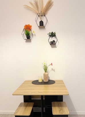 Una mesa de madera con un tapete circular negro, acompañada por dos sillas negras, y tres macetas hexagonales fijadas a la pared con diversas plantas y flores.