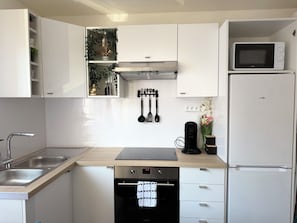 Une cuisine moderne avec des meubles blancs, un four à micro-ondes encastré, une machine à café et un lave-vaisselle.